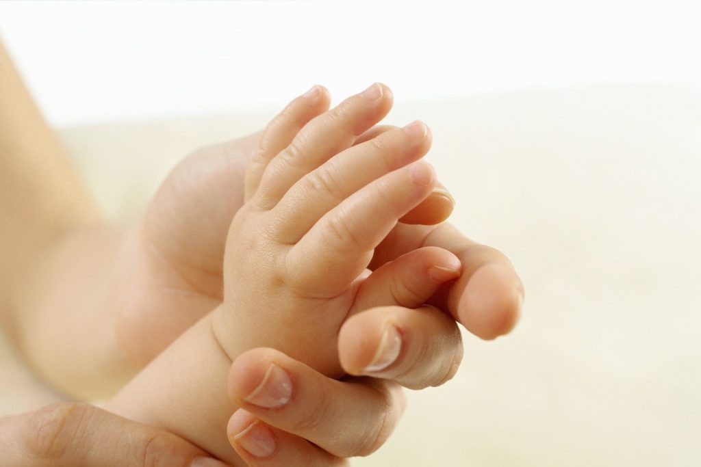 Gentle adult hand holding a newborn’s hand during egg donation journey in Greece.