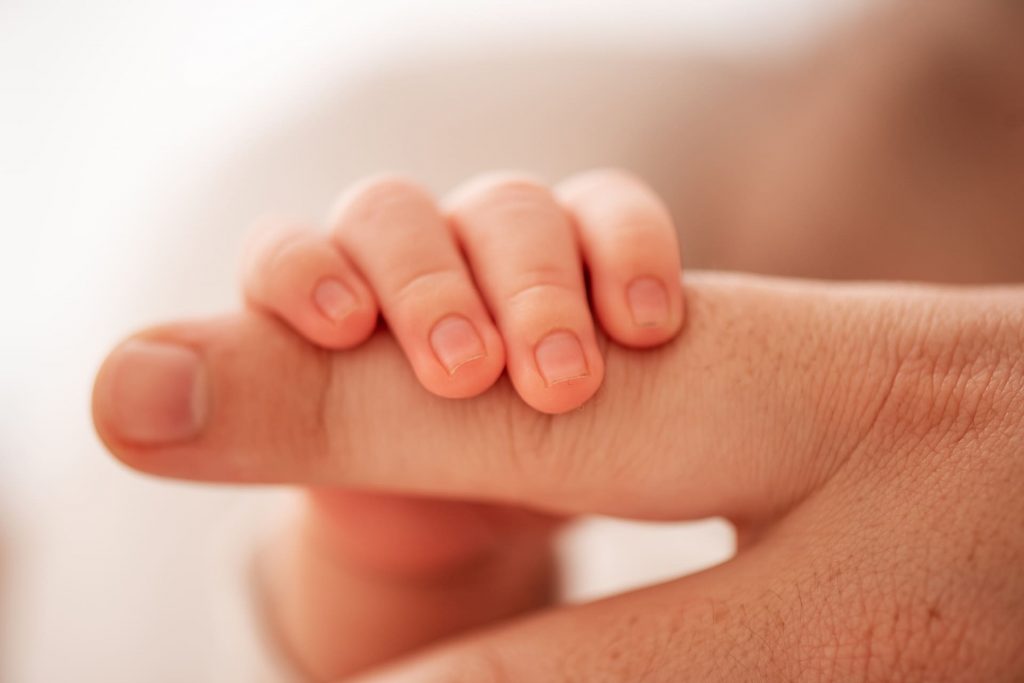 Kleines Babyhand greift Erwachsenenfinger — Symbol der Hoffnung nach erfolgreicher Eizellspende in Griechenland.
