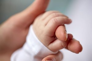 A newborn’s tiny hand gently holds an adult finger, symbolizing the successful IVF outcome after G-CSF endometrial treatment.