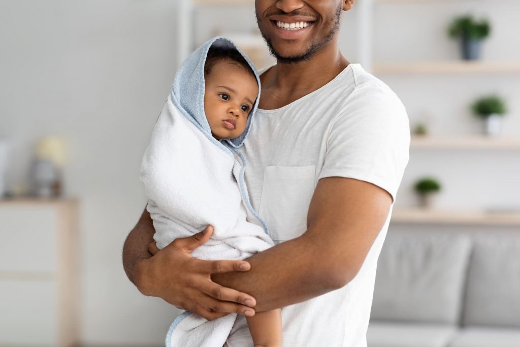 Ein lächelnder Vater hält sein eingewickeltes Neugeborenes – eine Darstellung der emotionalen Belohnung und des Bandes durch icsi-ivf-Familienplanung.