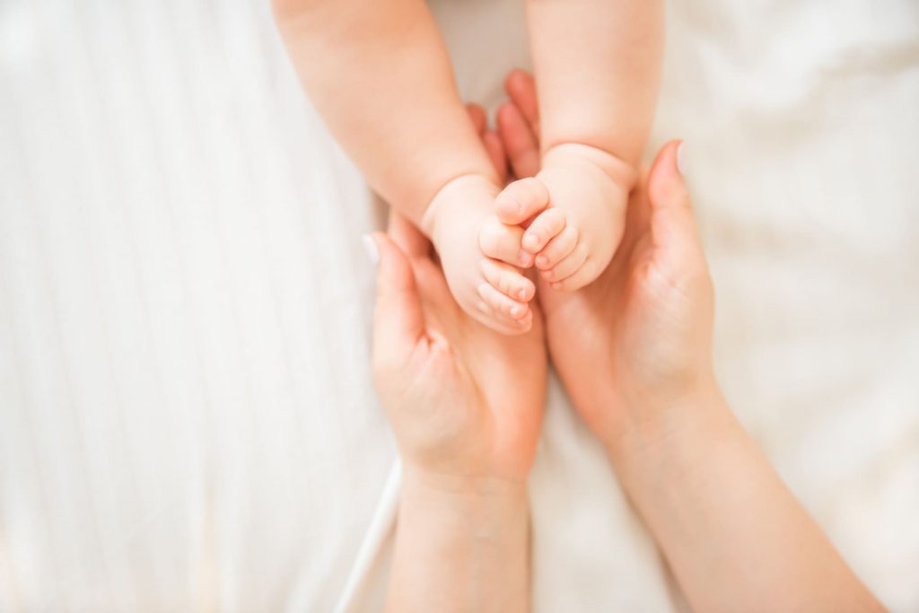 Sanfte haende halten die fuesse eines neugeborenen, symbolisieren pflege und den beginn des lebens nach erfolgtem ivf.