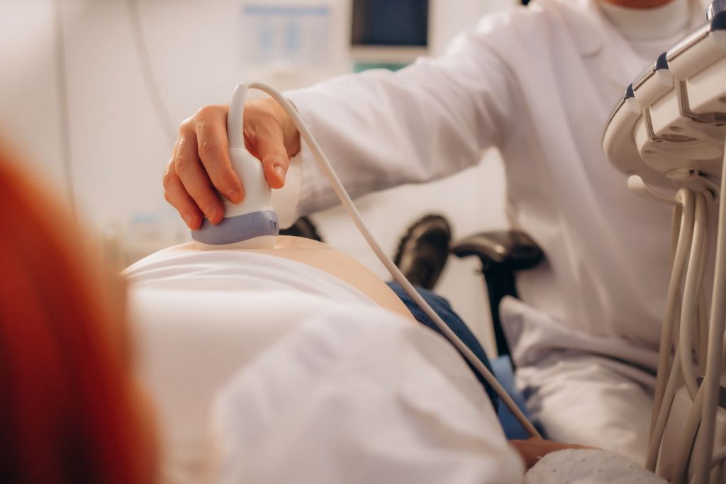 Doctor performs abdominal ultrasound on patient, monitoring early pregnancy progress after successful IVF sperm freezing.