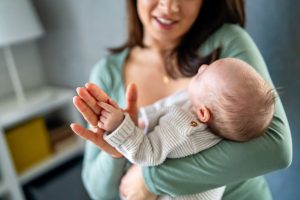 A smiling mother gently holds her newborn’s hand near her face, a tender moment after mini IVF success.