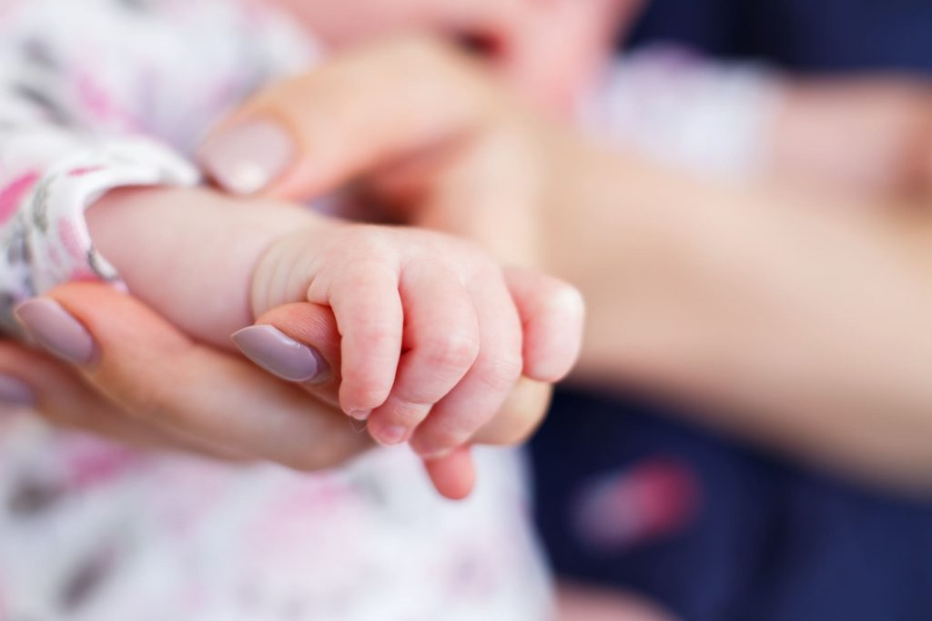 Eine Mutter haelt sanft die kleine Hand ihres Neugeborenen, ein zarter Moment, der die emotionale Belohnung nach Mini-IVF zeigt.
